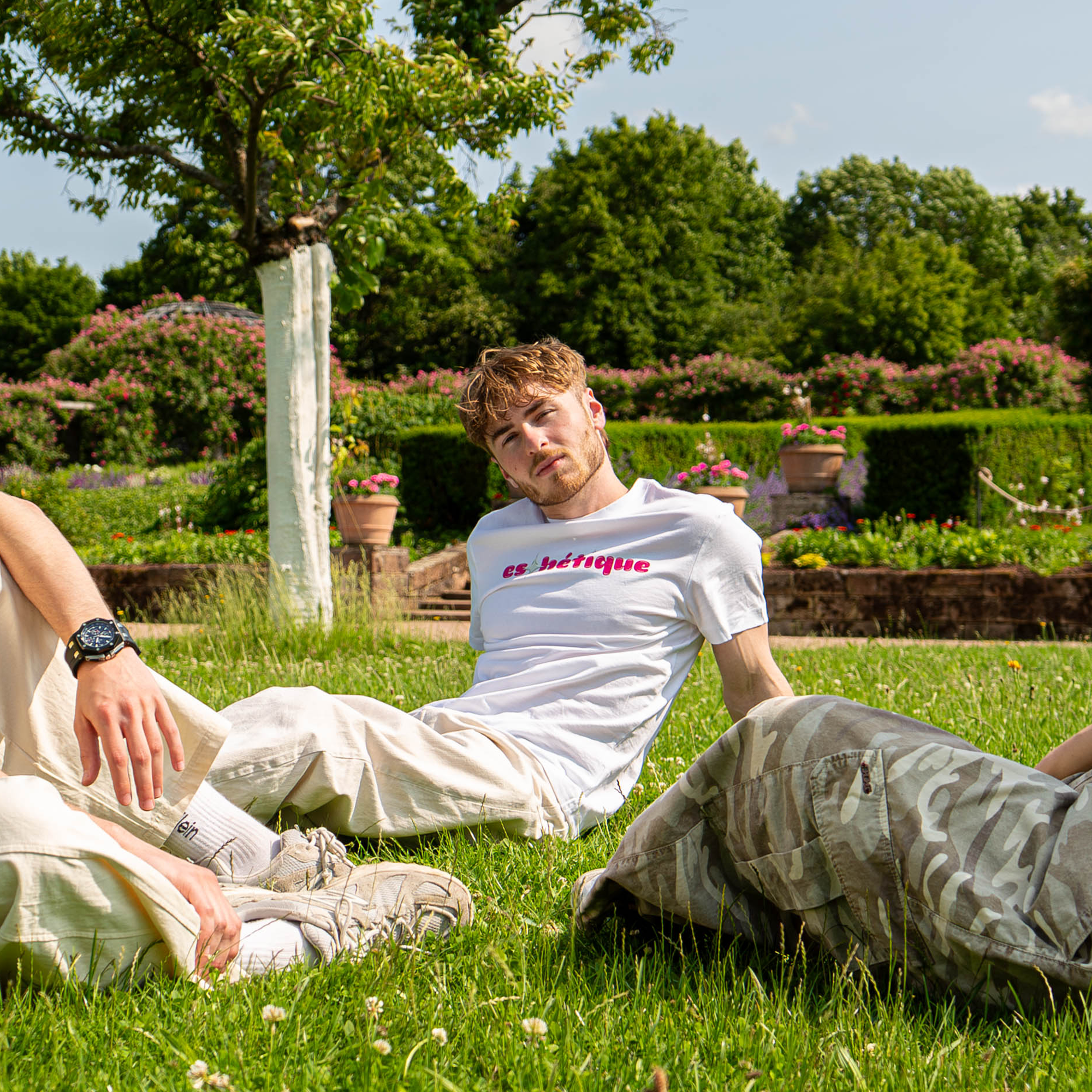 Weißes estclo T-Shirt mit pinkem ‚eshétique‘-Print, getragen im lässigen Picknick-Look auf einer Wiese